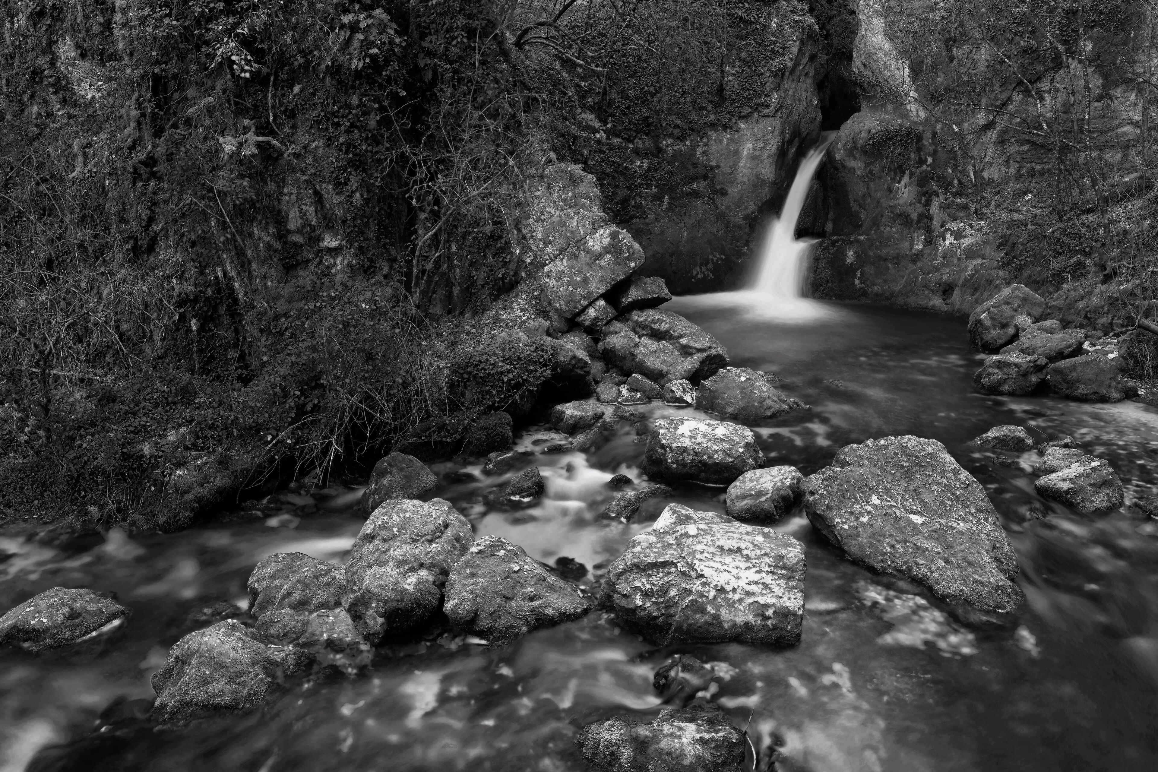 A black and white stream flowing through a rocky gorge with a waterfall.