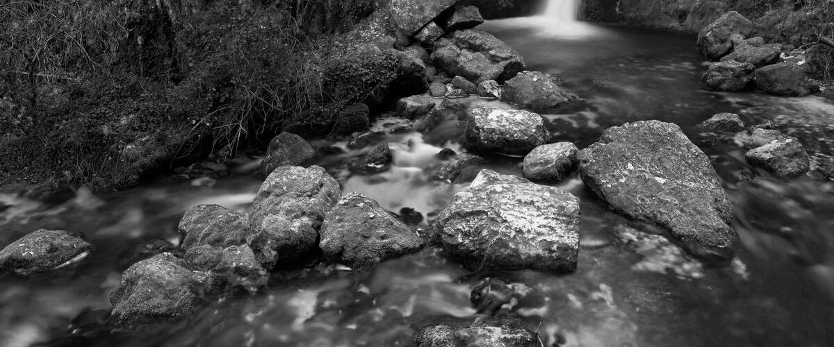 A black and white stream flowing through a rocky gorge with a waterfall.