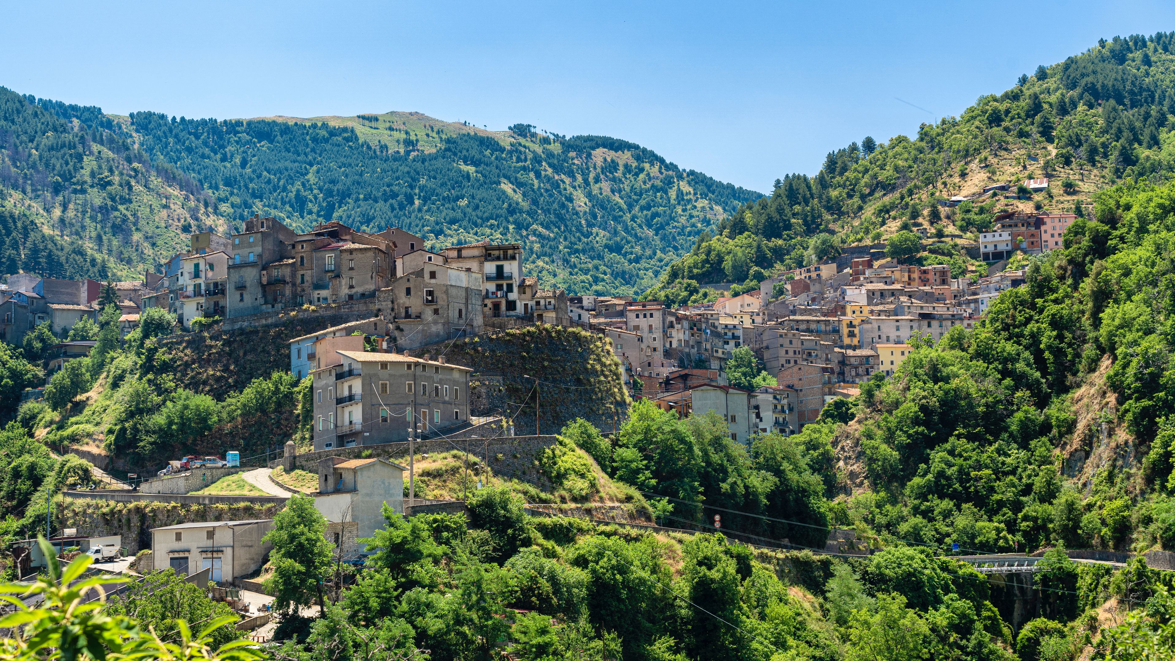 Un village perché sur une colline, avec des bâtiments nichés au milieu d’une végétation luxuriante et de collines.
