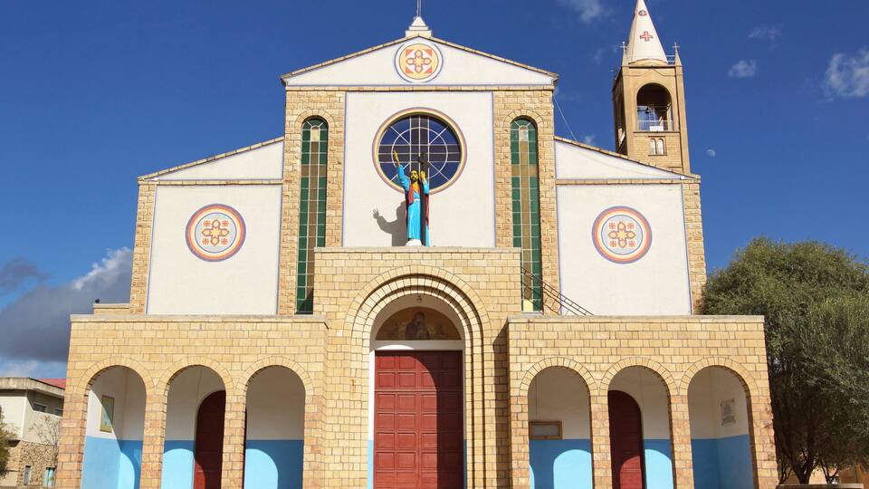 A church with a bell tower, arched windows, and a large circular window with a figure.