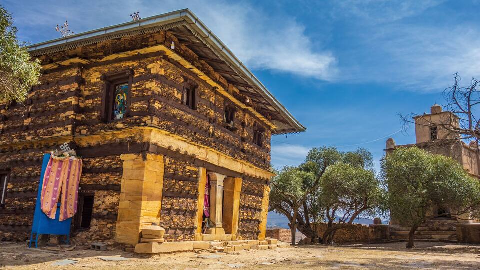 A historic stone building with a tiled roof, a balcony, and a colorful cloth hanging on the wall.