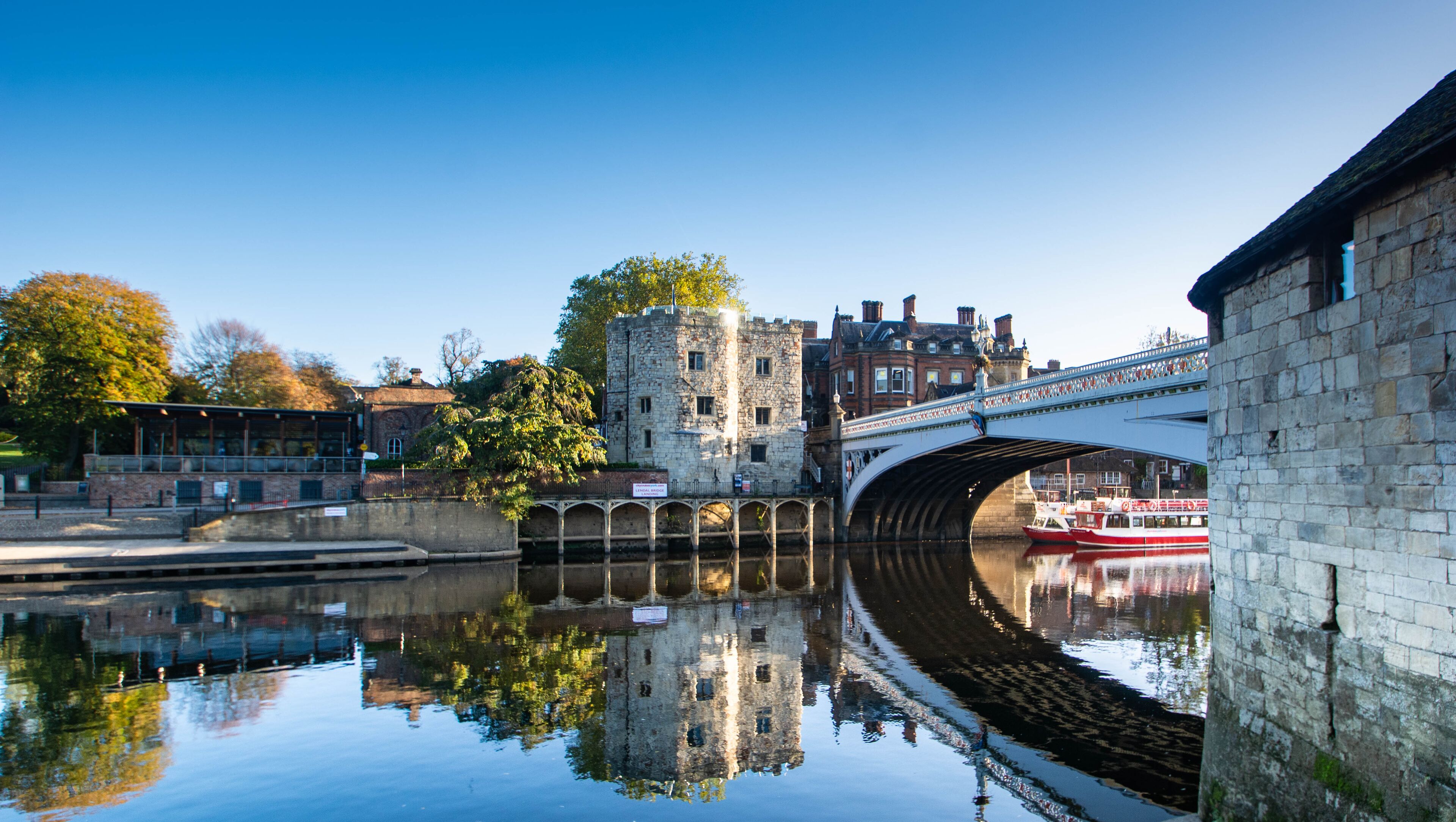 A stone bridge over a calm river reflecting buildings and trees.