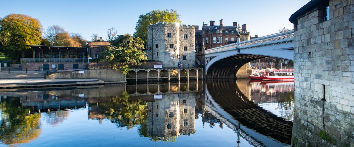 A stone bridge over a calm river reflecting buildings and trees.