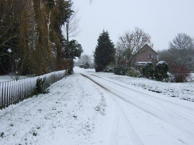 A snow-covered rural road with houses and trees on either side.