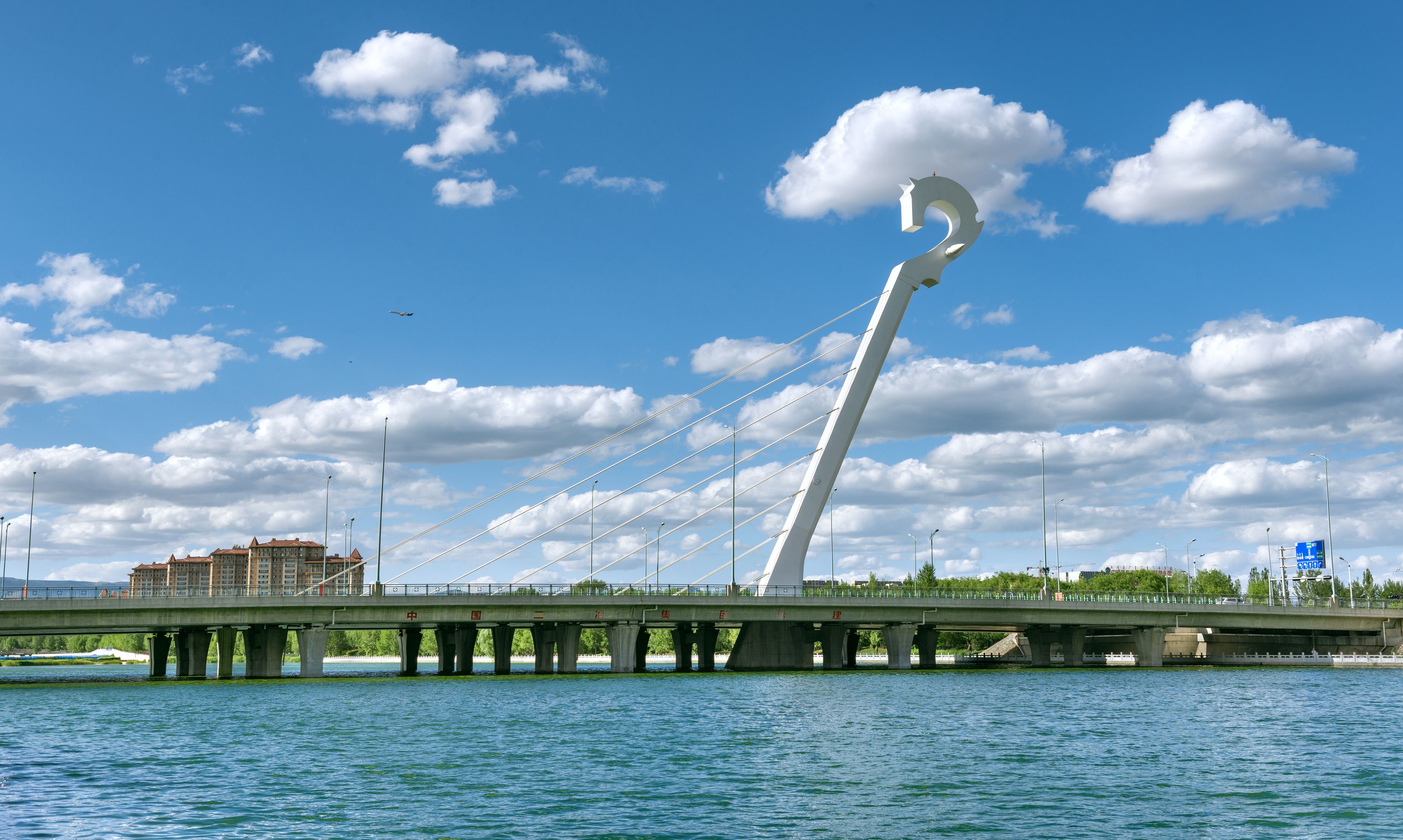 Uma ponte com um arco branco característico sobre um rio, com edifícios e vegetação ao fundo.