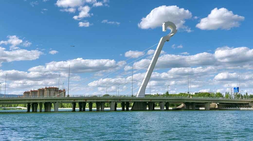 Uma ponte com um arco branco característico sobre um rio, com edifícios e vegetação ao fundo.