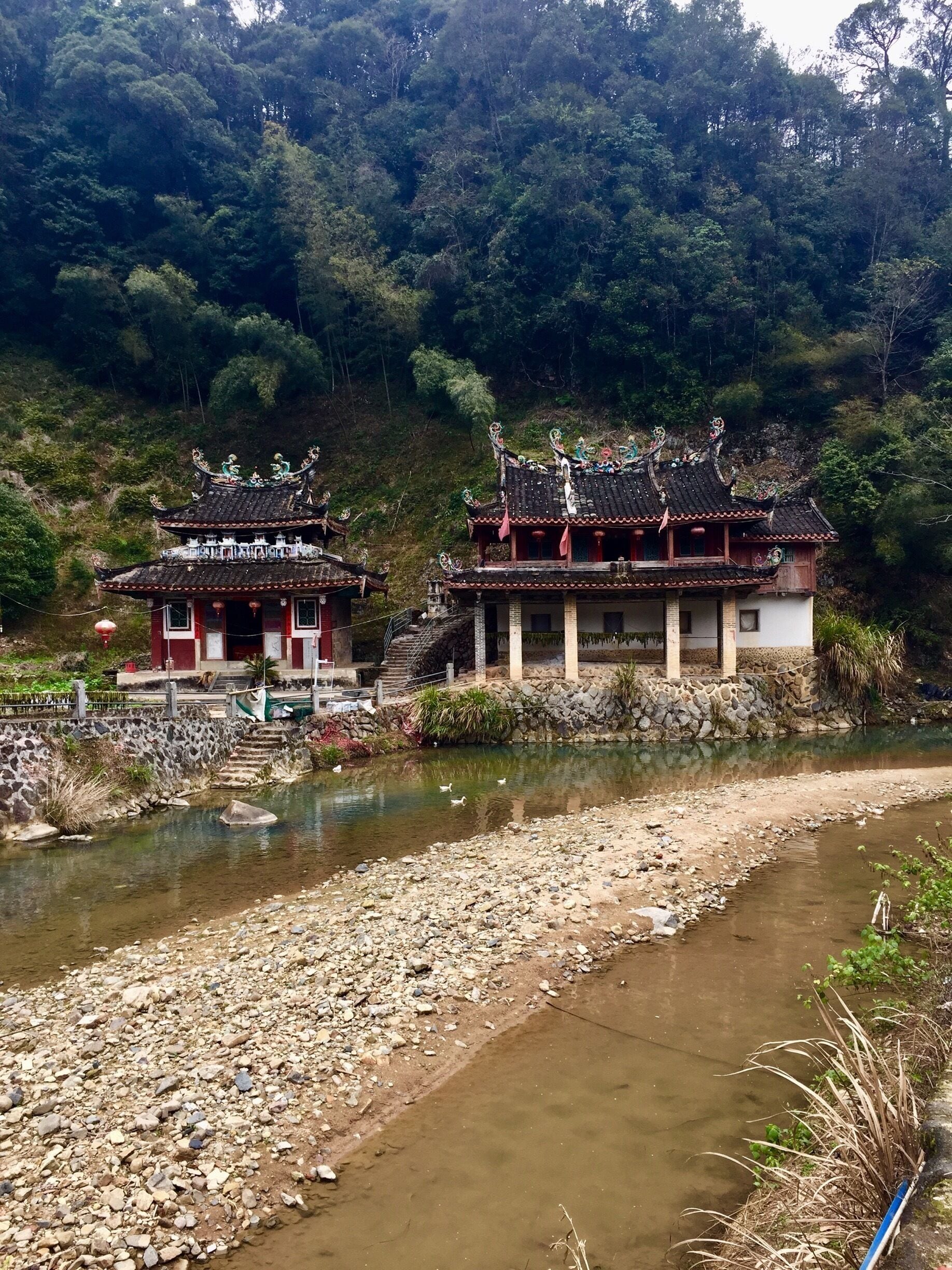 Um templo chinês tradicional com telhados ricamente decorados e um rio ao primeiro plano.