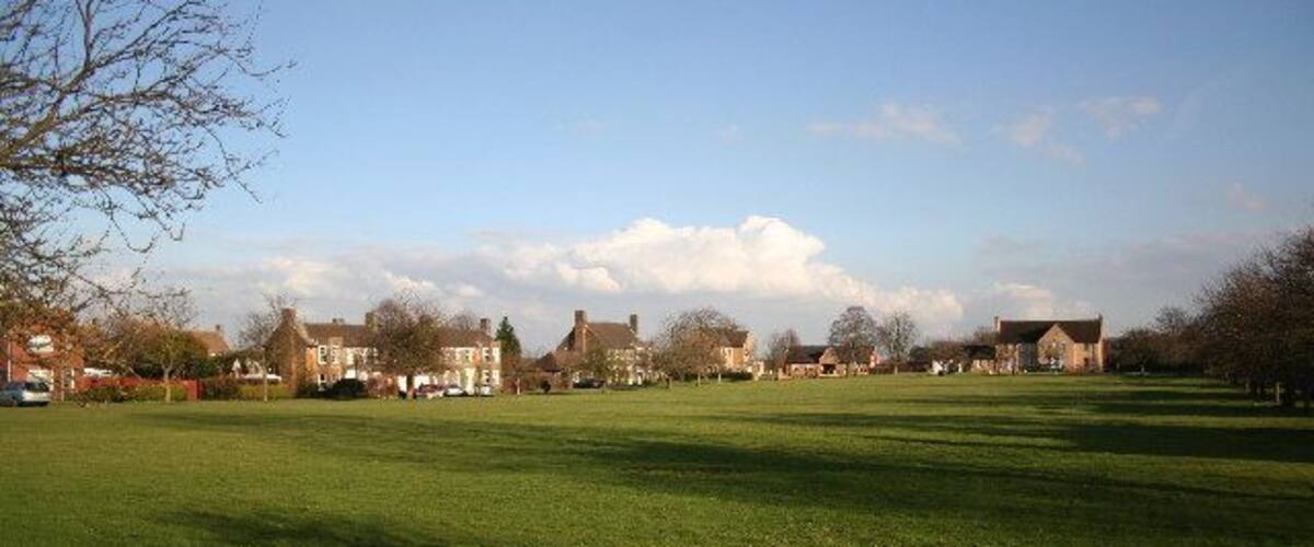 A green field with houses in the background.