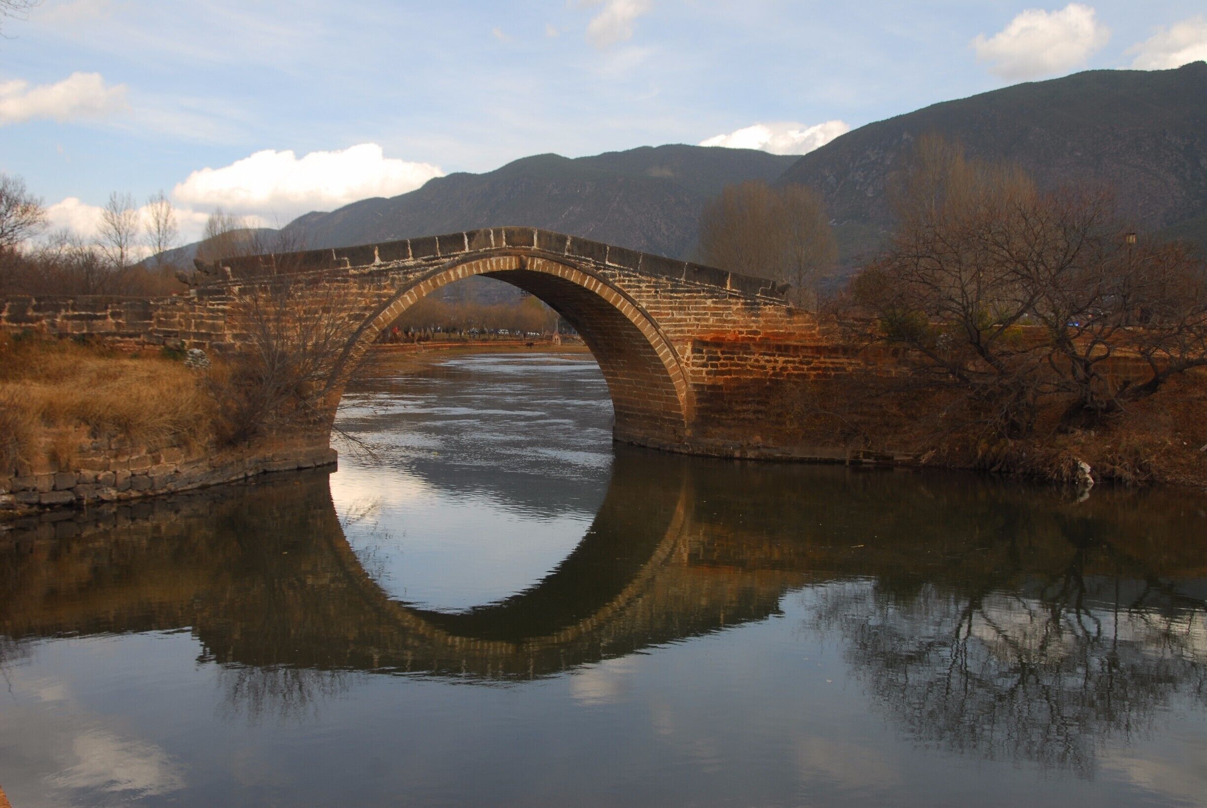 A stone bridge over a river with mountains in the background.