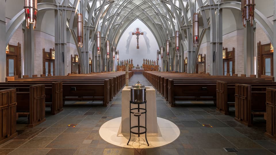 A church interior with a central altar, pews, and a cross at the far end.
