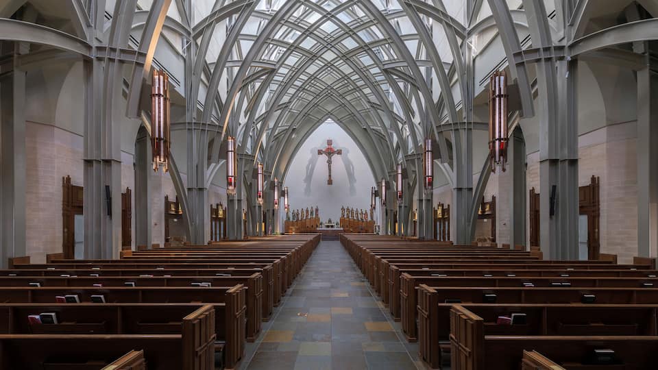 A church interior with high vaulted ceilings, wooden pews, and a central crucifix.