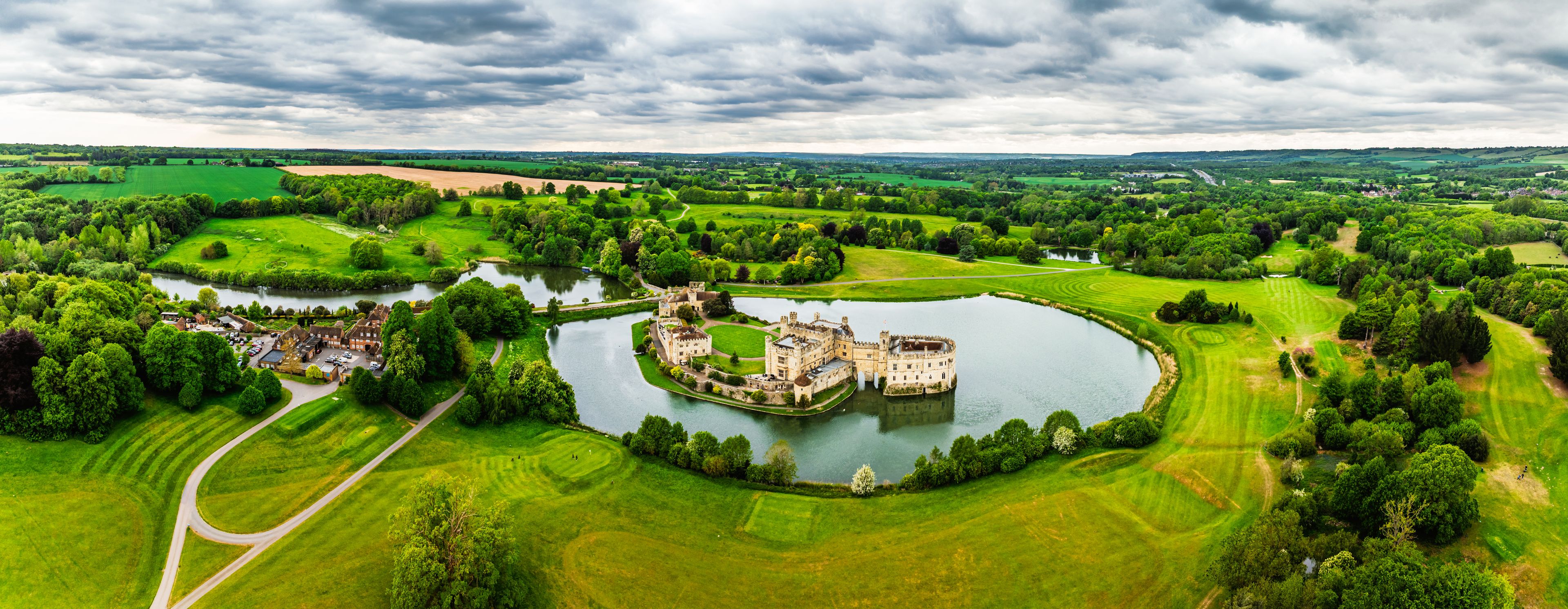 Un château entouré d’un lac et de vastes prairies verdoyantes.