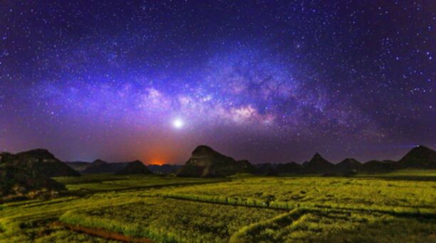 A starry night sky over a green field with distant mountains.