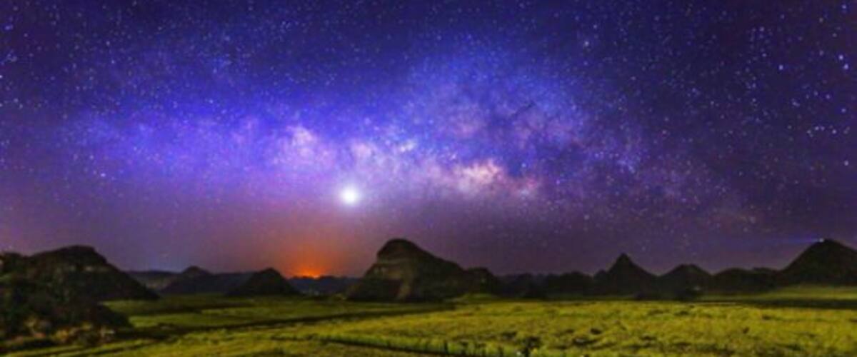 A starry night sky over a green field with distant mountains.