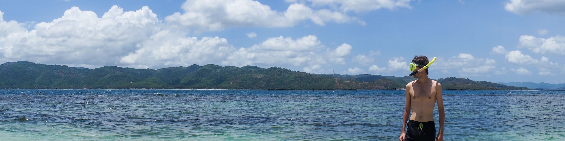 A person snorkeling in clear blue water with a mountainous landscape in the background.