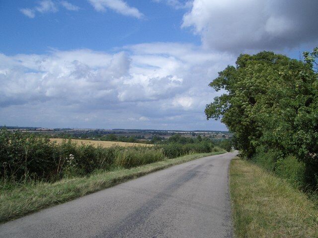 The Country Road to Newton Blossomville This road drops down the hill into Newton Blossomville from the south, over a disused railway bridge and arriving at the T-junction shown in grid square SP9251. This view also looks over the Great Ouse Valley near Lavendon.