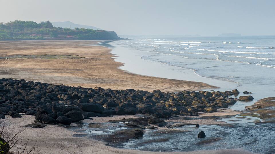 A coastal landscape with rocky shores, a sandy beach, and a distant mountain range.