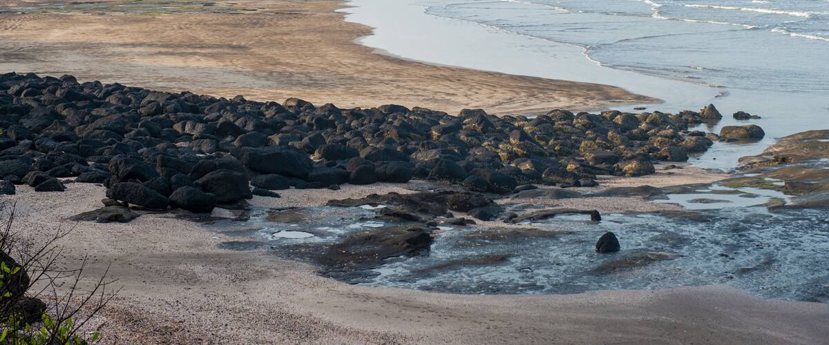 A coastal landscape with rocky shores, a sandy beach, and a distant mountain range.