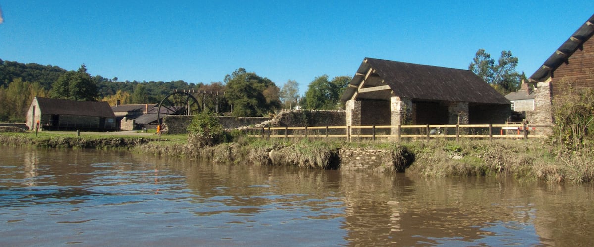 A rural landscape with a water wheel, stone buildings, and a river.