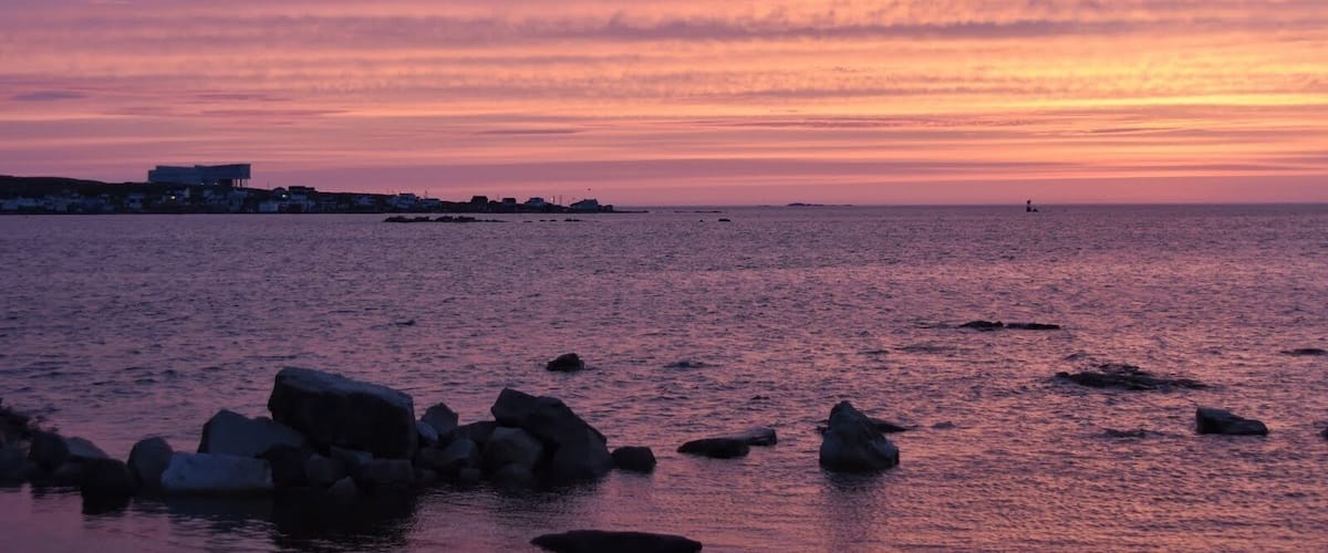 A sunset over a coastal area with rocky outcrops and a distant shoreline with buildings.