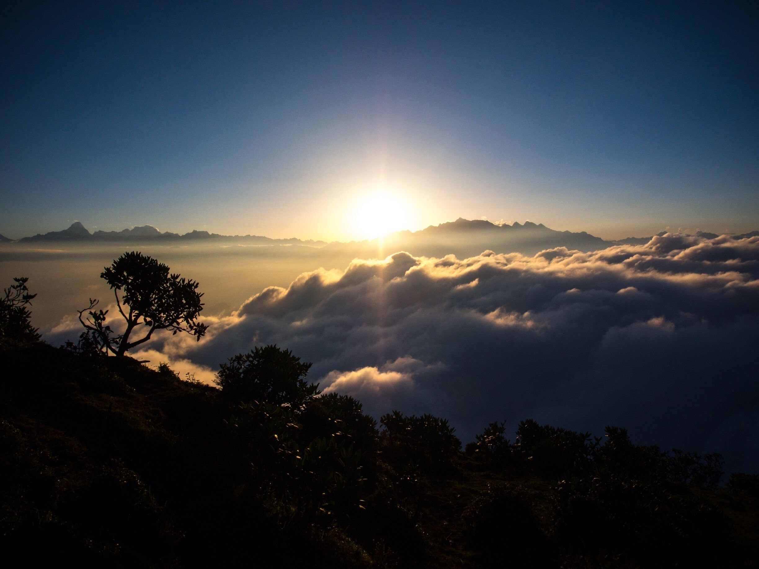 A sunrise over a mountain range with clouds below.