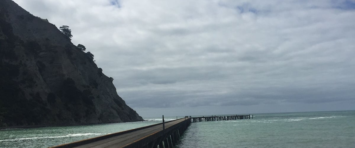 A wooden pier extending into calm waters, surrounded by rocky cliffs and a cloudy sky.