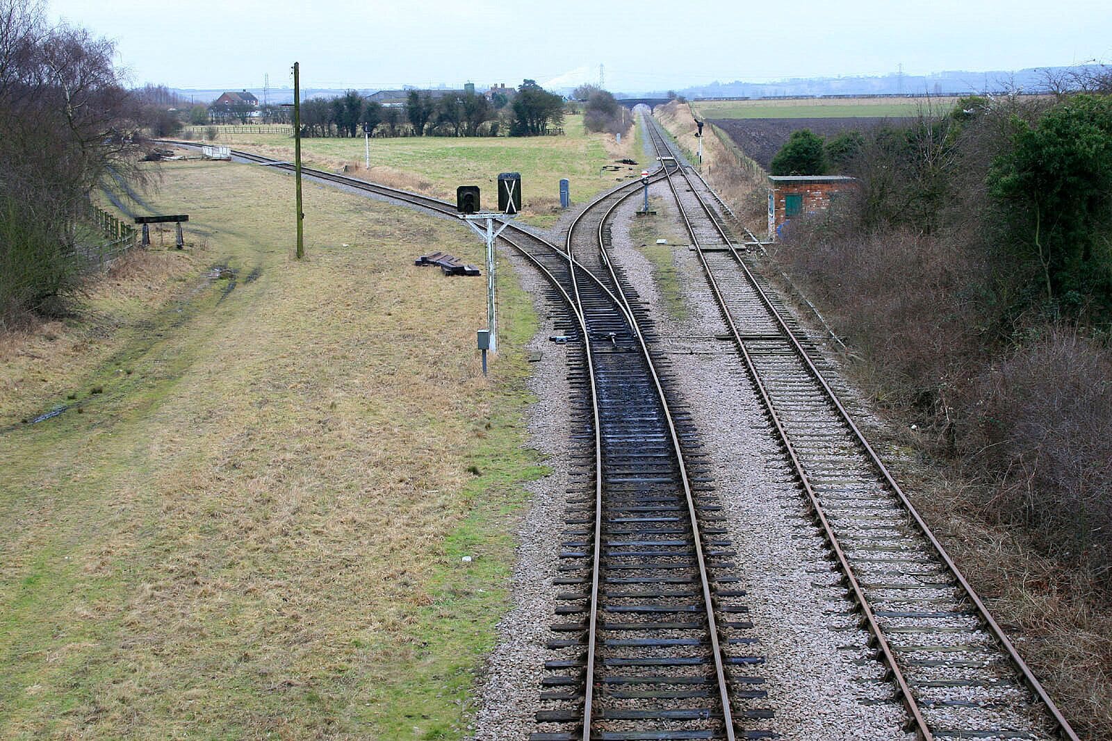 Railway tracks curving through a rural landscape with grassy fields and sparse trees.