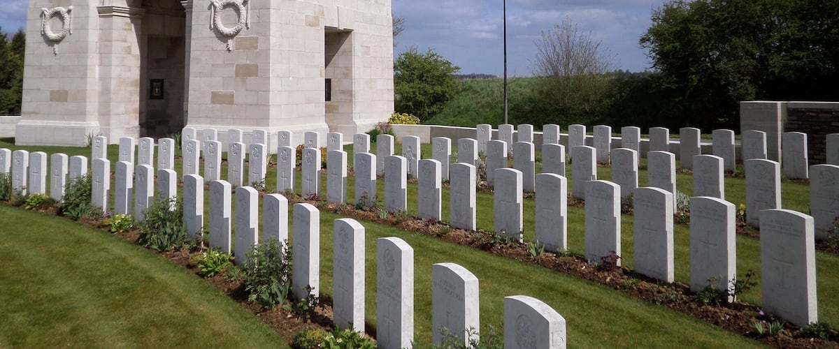 A large stone monument with a dome and arched entrance, surrounded by rows of white headstones in a cemetery.