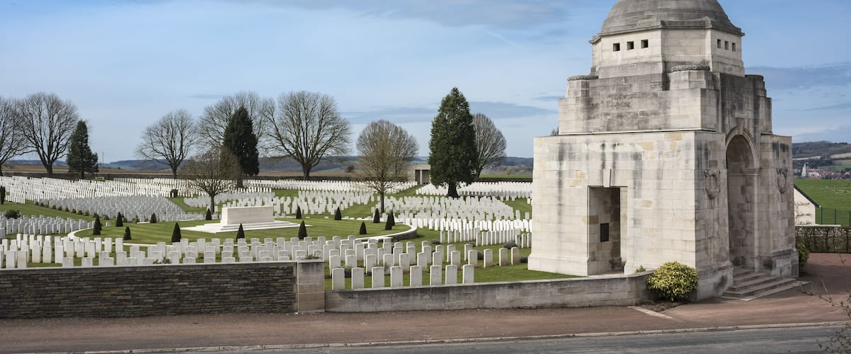 A cemetery with numerous white headstones, a central monument, and a clear sky.