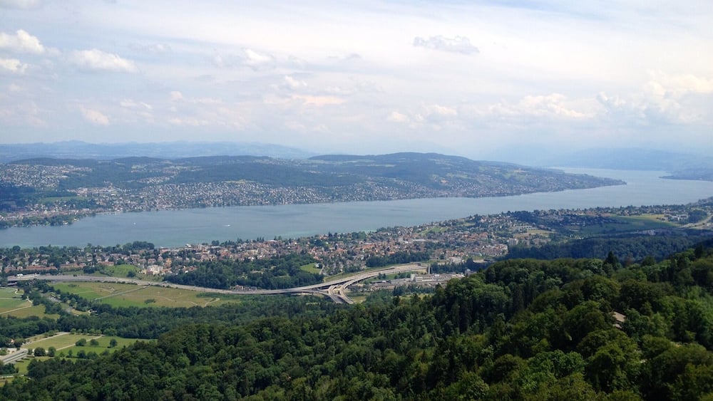 Eine Küstenstadt, umgeben von Hügeln und dichten Wäldern, mit einer weiten Wasserfläche.