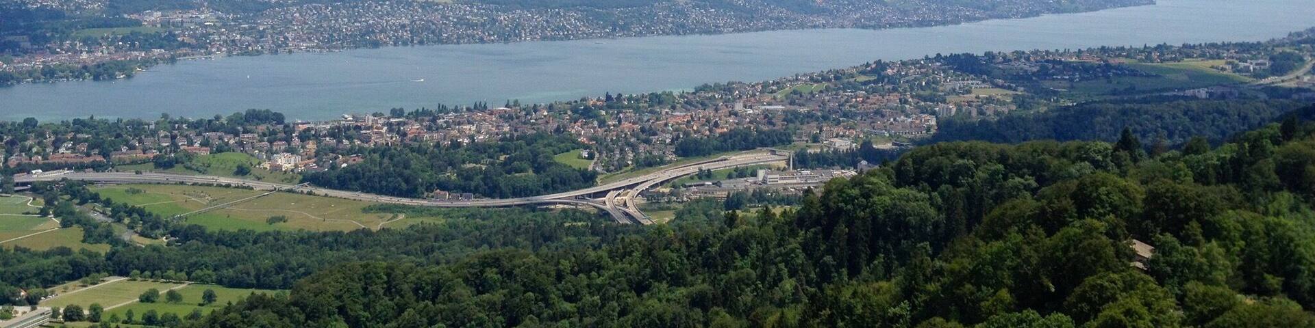 A coastal city with a large body of water, surrounded by hills and dense forests.