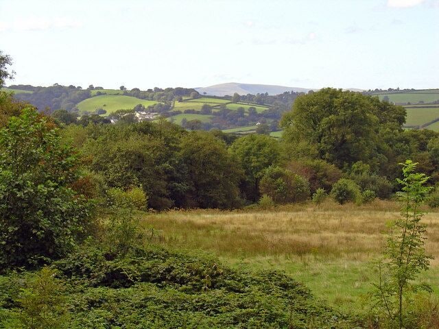 A rural landscape with rolling hills, dense forests, and a grassy field.