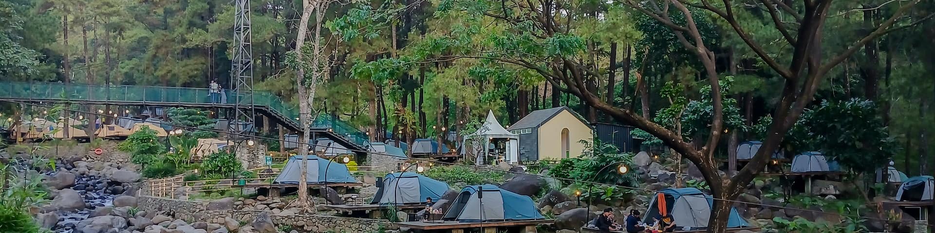 Glamping tents in Jolotundo, Nganjuk, East Java, surrounded by forest, rocks, and a flowing stream.