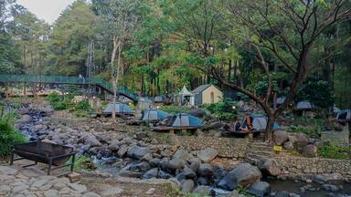 Glamping tents in Jolotundo, Nganjuk, East Java, surrounded by forest, rocks, and a flowing stream.
