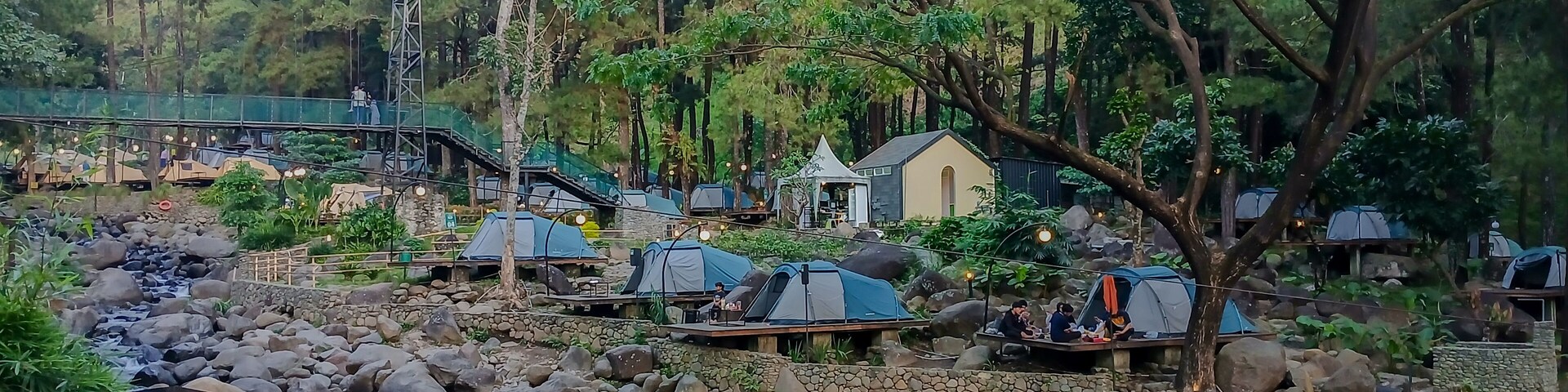 Glamping tents in Jolotundo, Nganjuk, East Java, surrounded by forest, rocks, and a flowing stream.