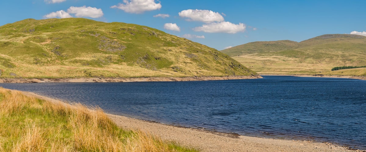 A lake surrounded by green hills with a clear sky.