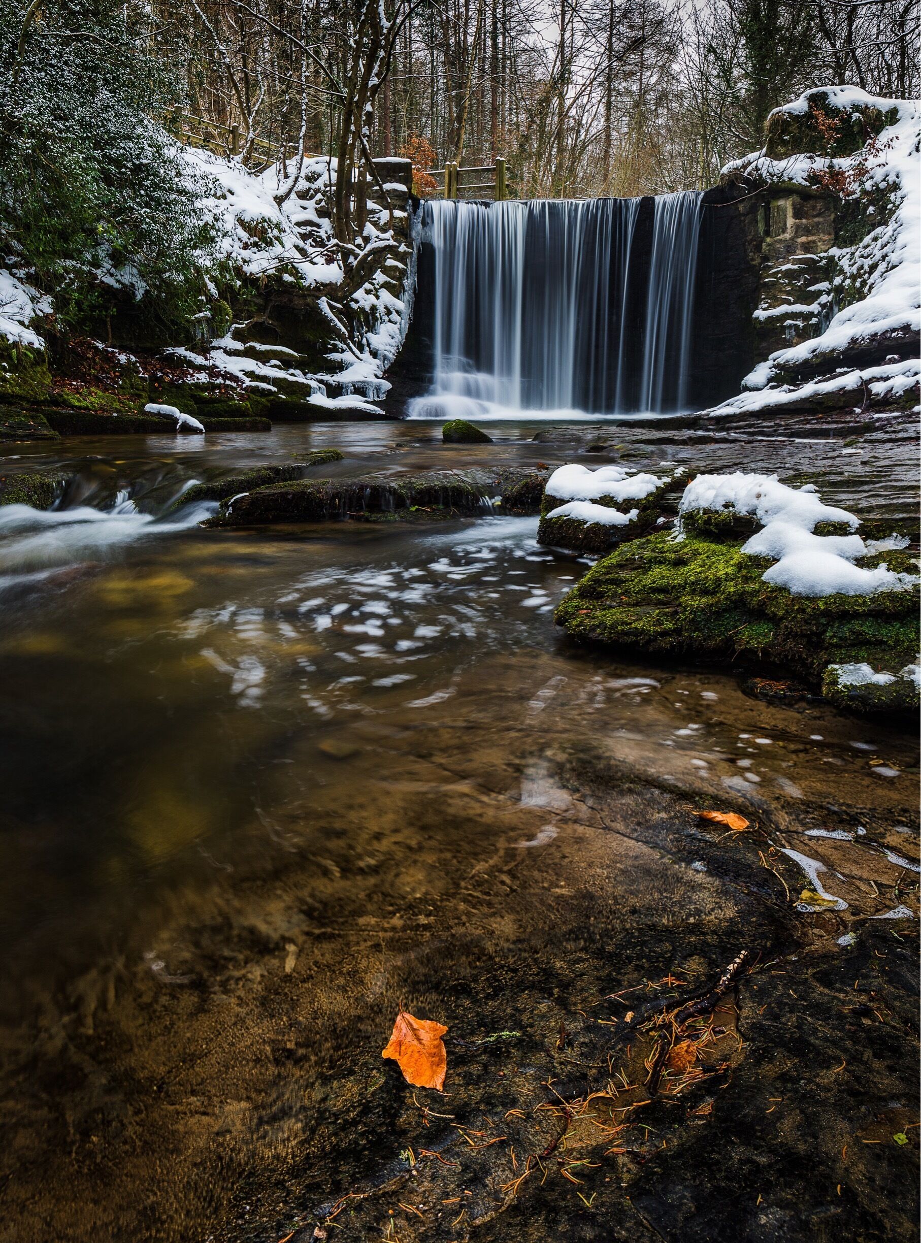 A waterfall in a forested area with snow-covered rocks and a clear stream.