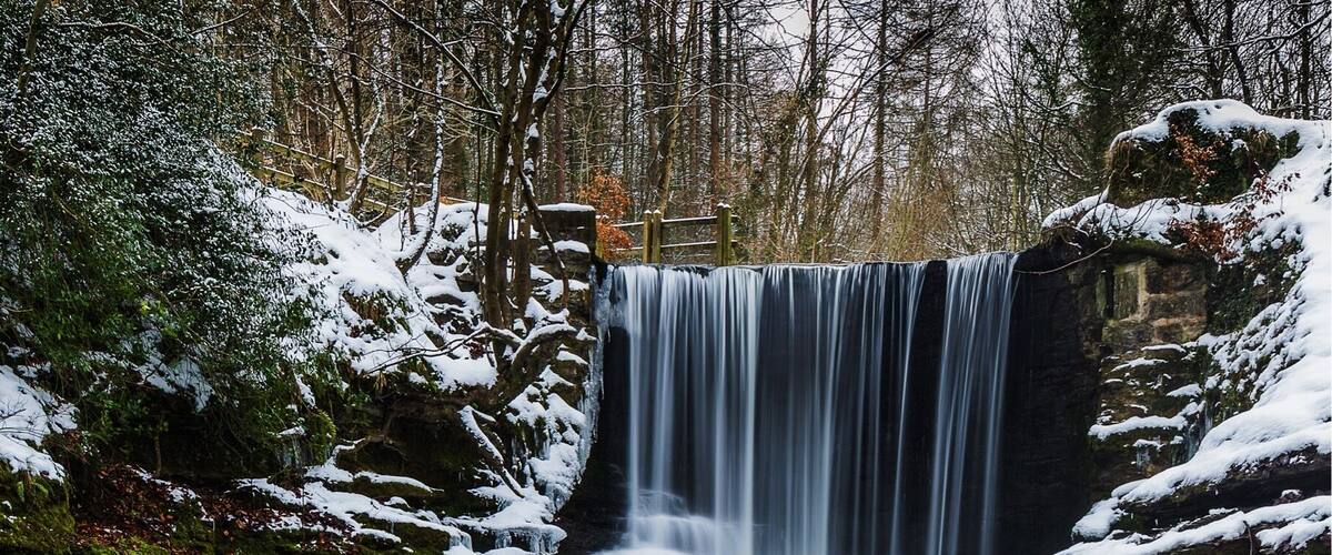 A waterfall in a forested area with snow-covered rocks and a clear stream.