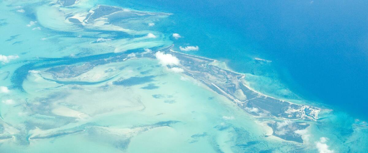 An aerial view of a coastal area with clear blue waters, a sandy beach, and a small settlement with buildings.