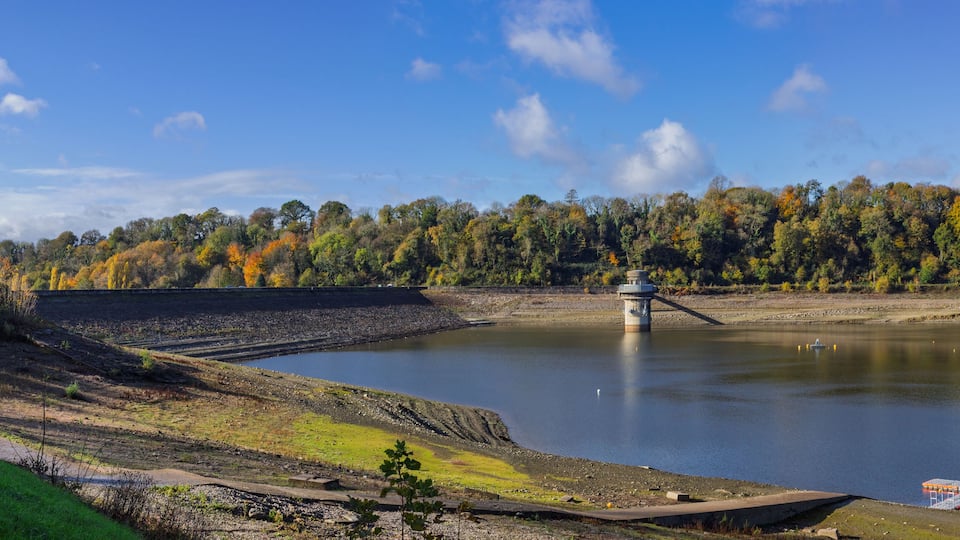 A dam with a lock system, a calm lake, and a forested hillside.
