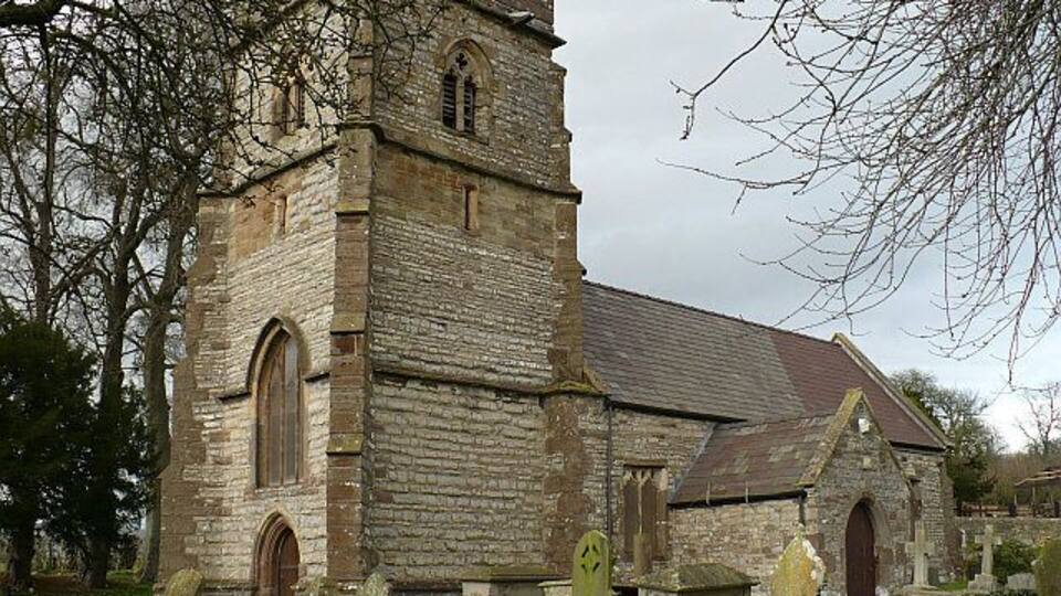 Una iglesia histórica de piedra con una alta torre y ventanas de arco.