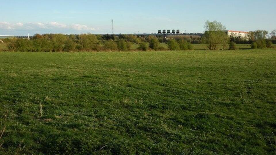 Un campo cubierto de hierba con árboles y un edificio a lo lejos.