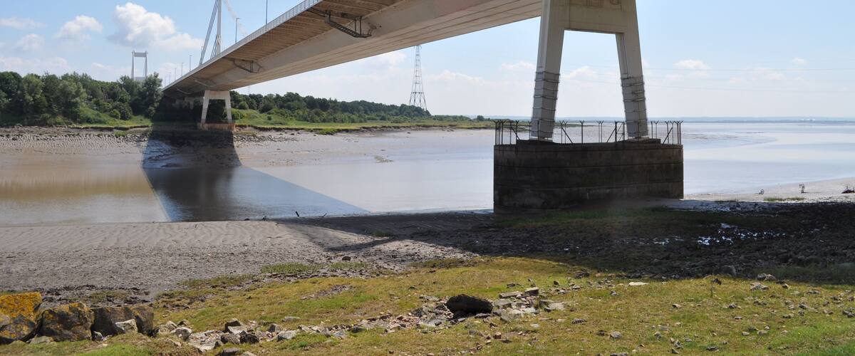 A bridge over a river with a sandy shore and greenery in the background.