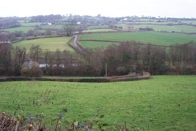 Rolling green fields, a winding road, and distant houses.