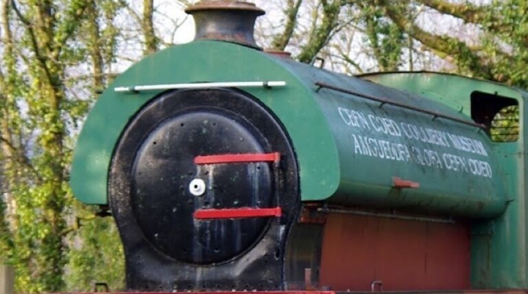 A full size derelict steam locomotive on the side of the road in the Cefn Coed colliery museum.
