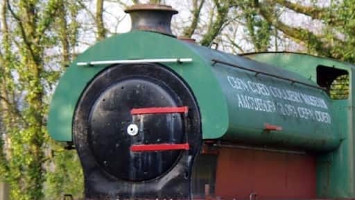 A full size derelict steam locomotive on the side of the road in the Cefn Coed colliery museum.