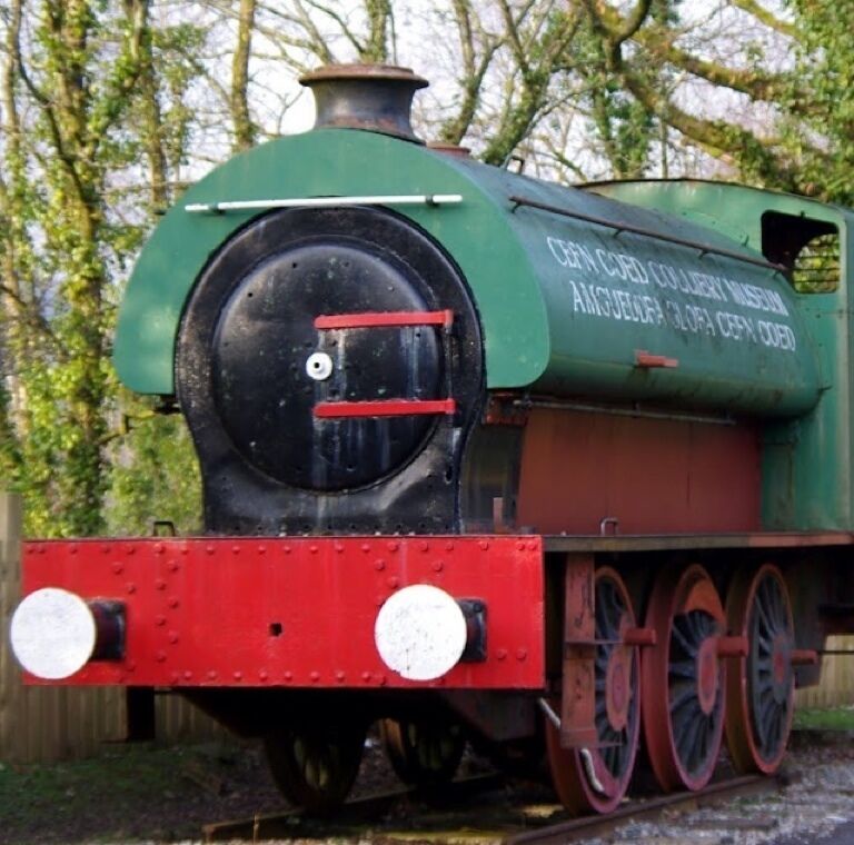 A green steam locomotive with red wheels and white headlights, parked outdoors.