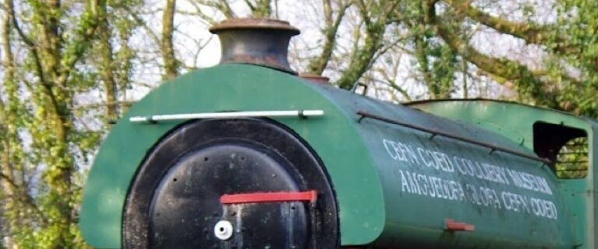 A green steam locomotive with red wheels and white headlights, parked outdoors.