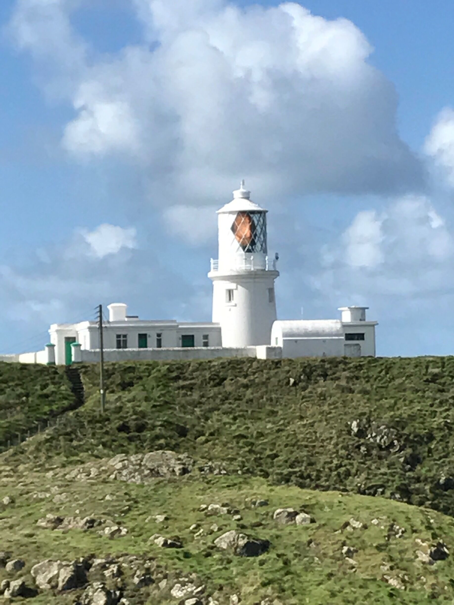 A white lighthouse with a diamond-patterned window on a hill.