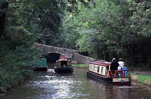 A narrow canal with boats, a stone bridge, and dense greenery.